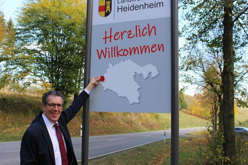 HERZLICH WILKLKOMMEN BEI UNS: Landrat Peter Polta klebt den roten Positionspunkt für Söhnstetten auf die neue Willkommenstafel für auswärtige Besucher. Foto: Landratsamt